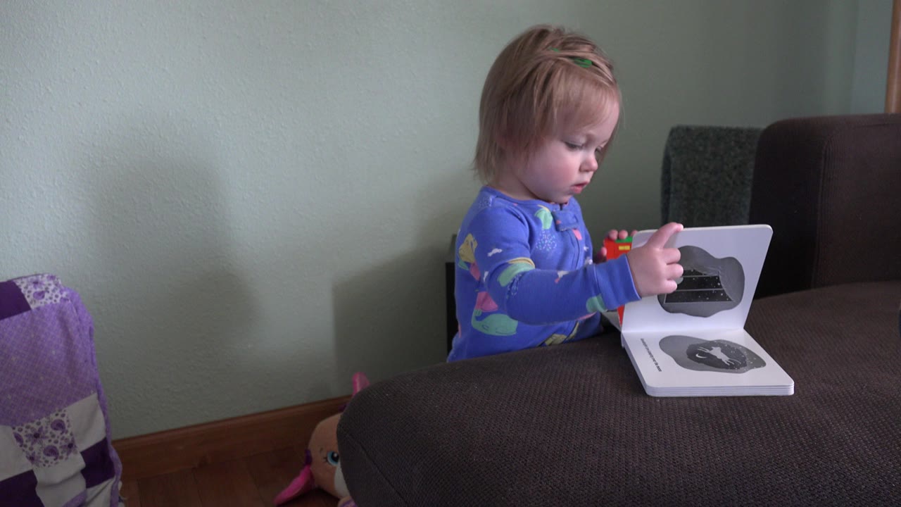 Toddler sits at a living room table looking down at an open board book.