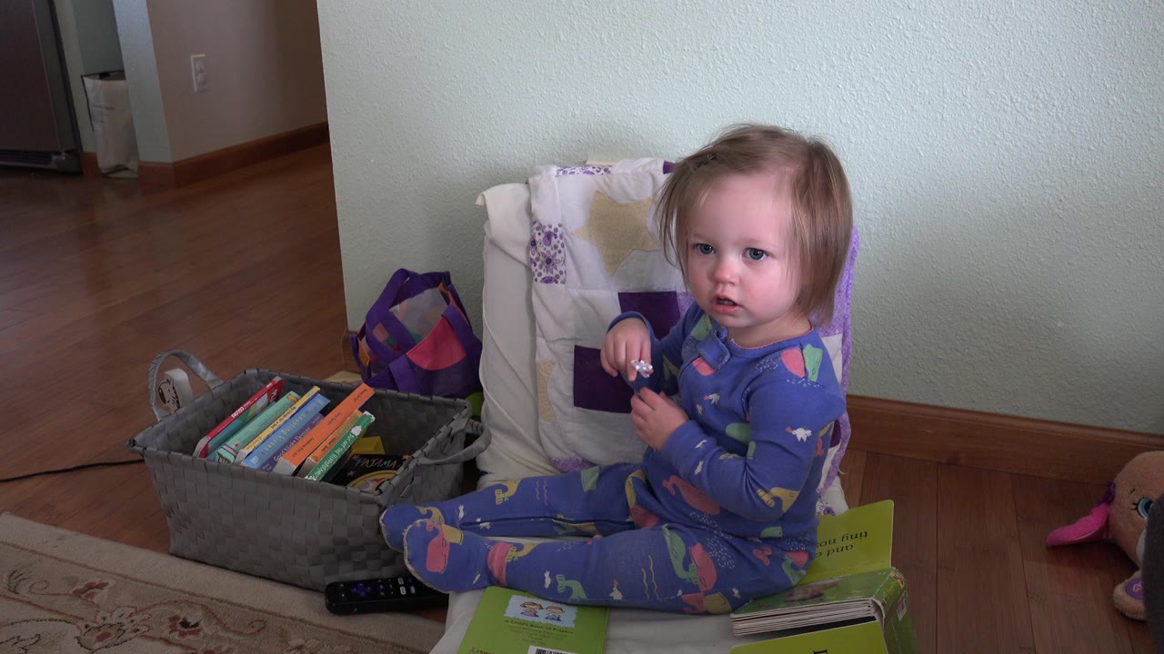 Young girl sitting beside a bin of books indoors.