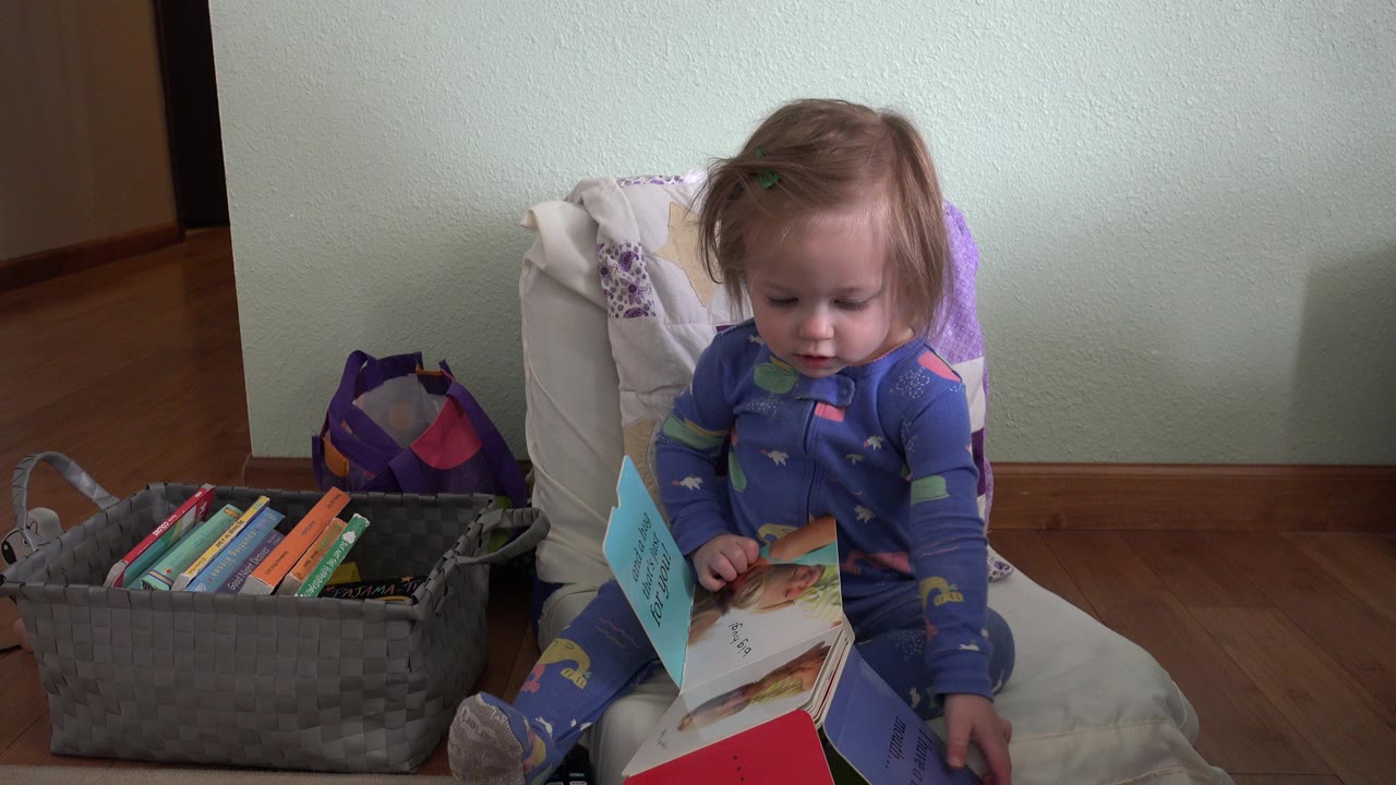 In Westminster, Colorado, the toddler remains seated on the chair, looking down at the open book while the gray book basket fills the left foreground.