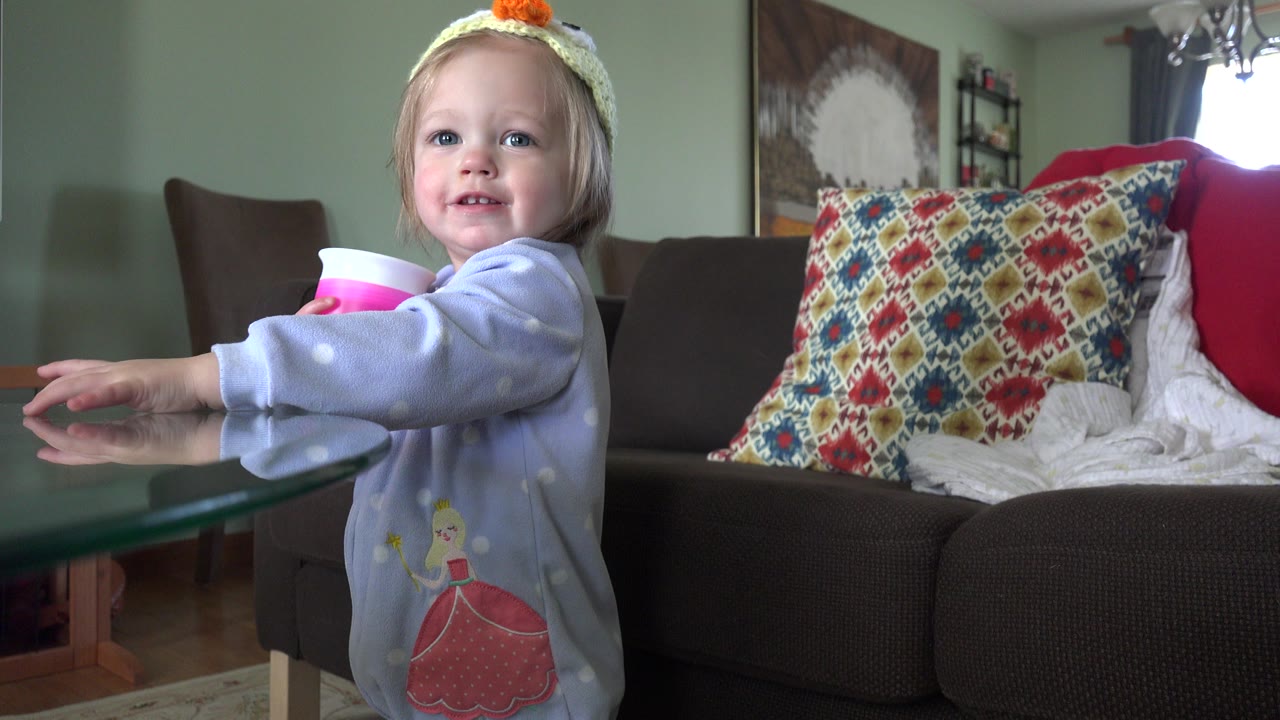 Young girl in princess pajamas holding a pink cup by a glass table.