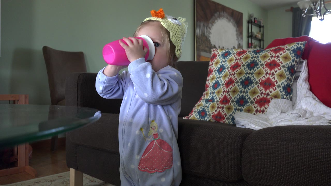 At 0:00, a baby in purple pajamas drinks from a pink cup beside a glass table in a Westminster, Colorado living room.