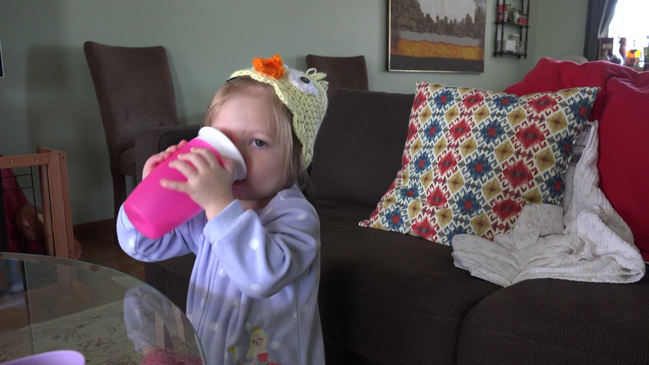 Toddler drinks from a pink cup at a glass table.