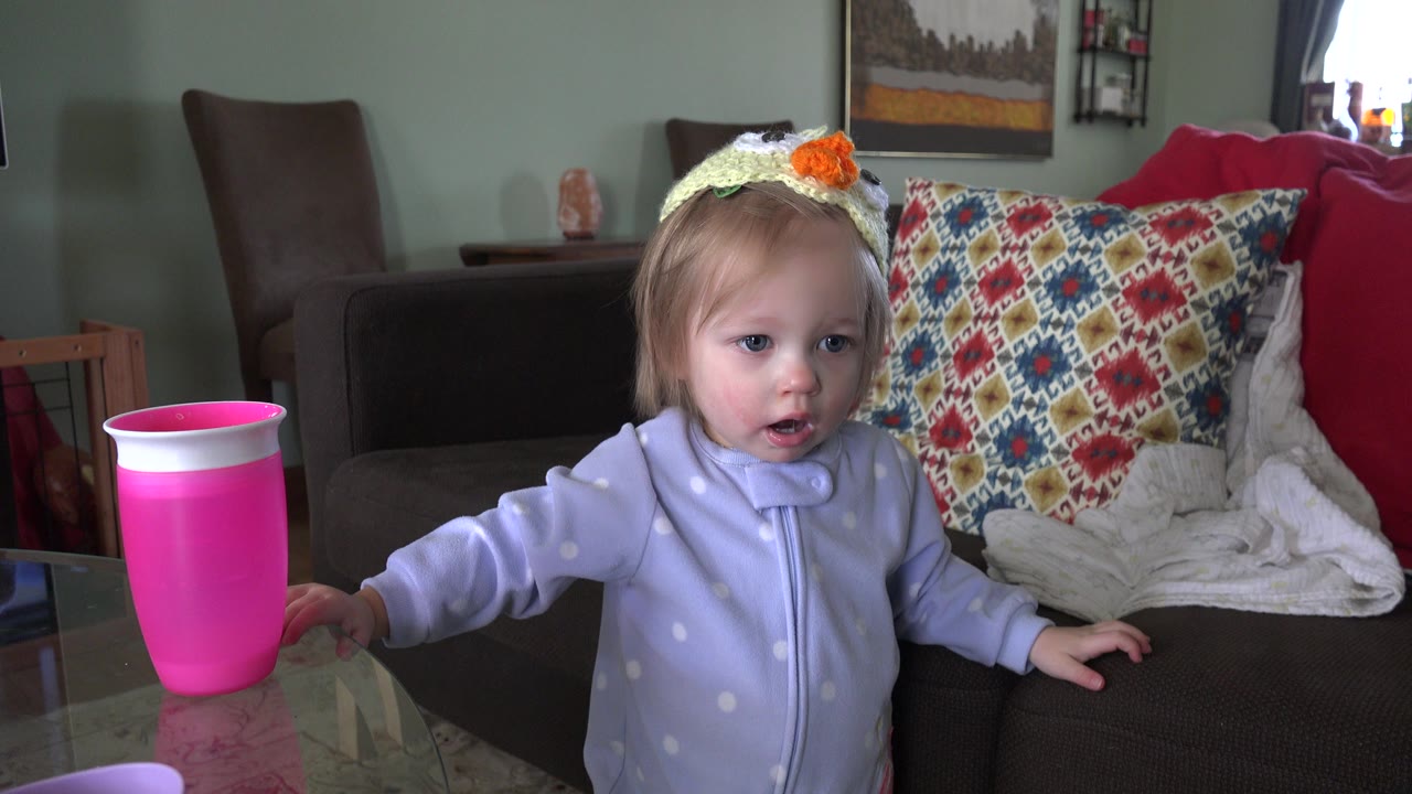 The toddler keeps one hand near the glass table and pink cup while looking ahead in the Westminster, Colorado home interior.