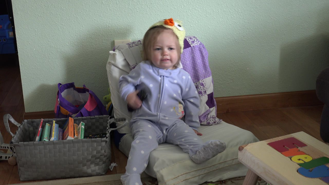 At 0:00 in Westminster, Colorado, a toddler in a pale purple outfit sits on a cushioned chair with a book basket and small table nearby.