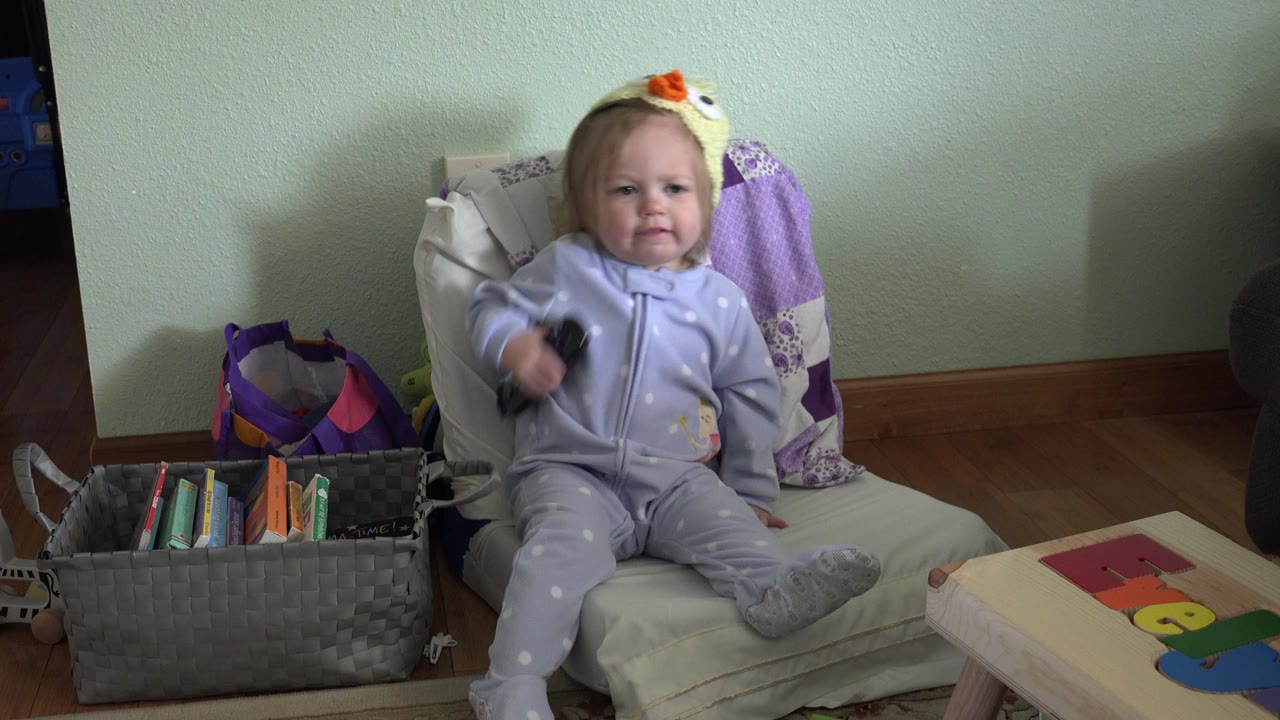 Toddler raises a black remote while sitting on a chair.