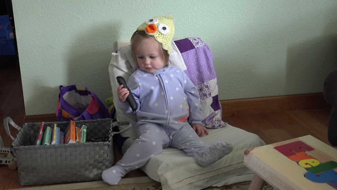 Toddler seated in a chair holding a remote control.