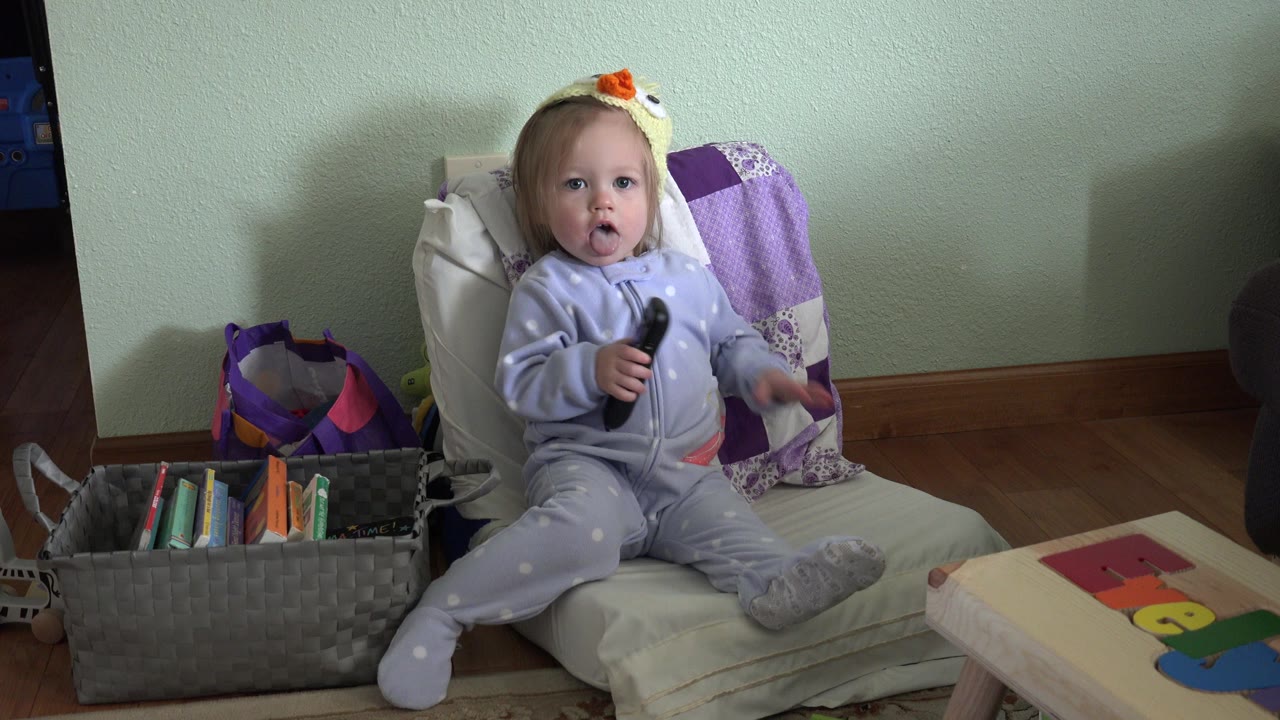 Toddler sitting on cushions holding a black remote.