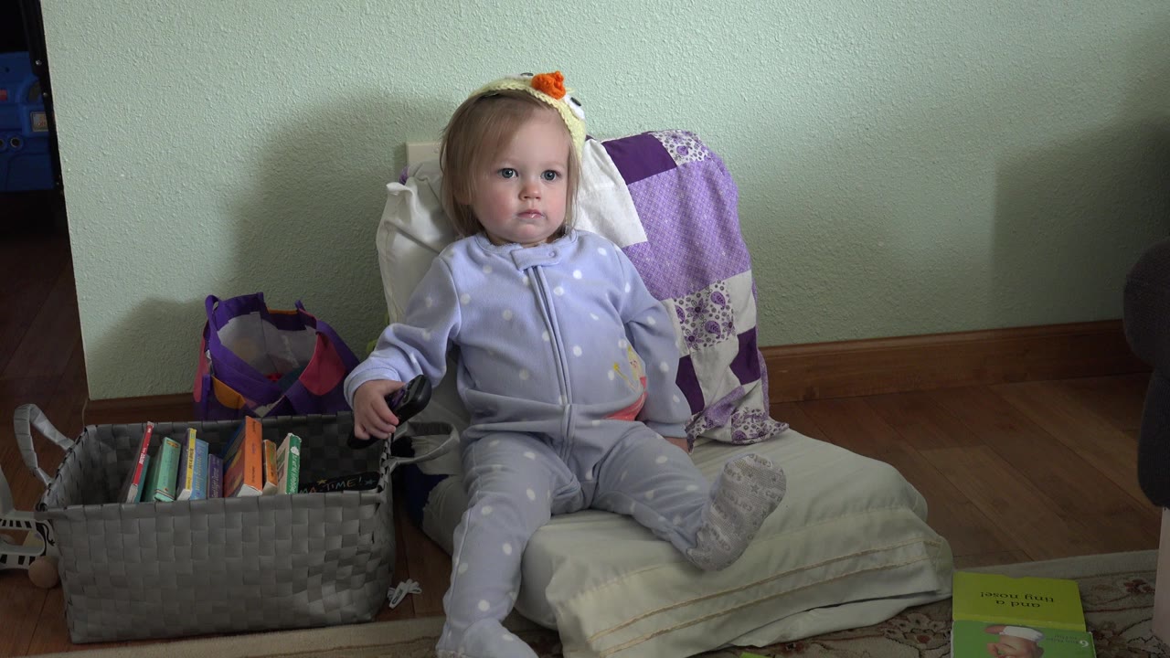 Toddler seated on a tiny chair with one hand near a basket handle.