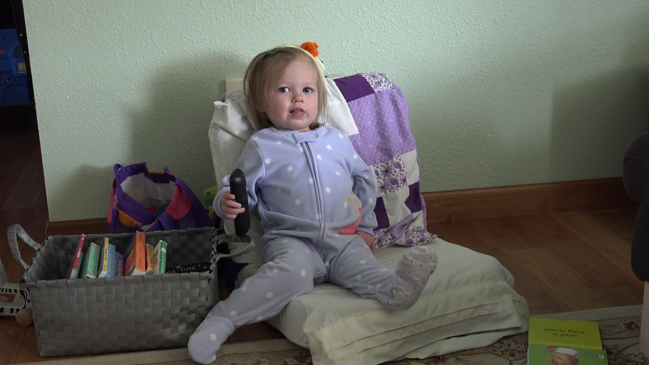 Baby girl seated on cushions beside a basket of books.