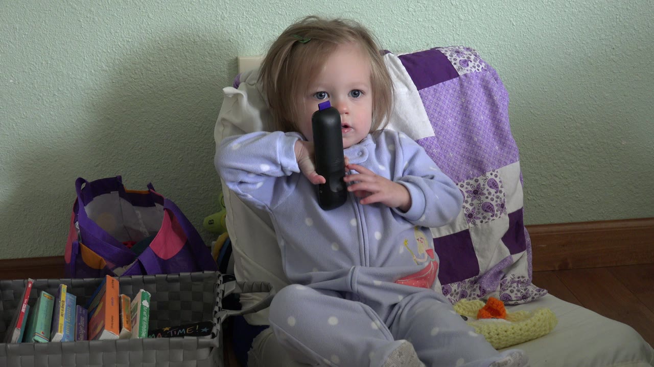 Toddler sitting on a chair holding a black remote control.