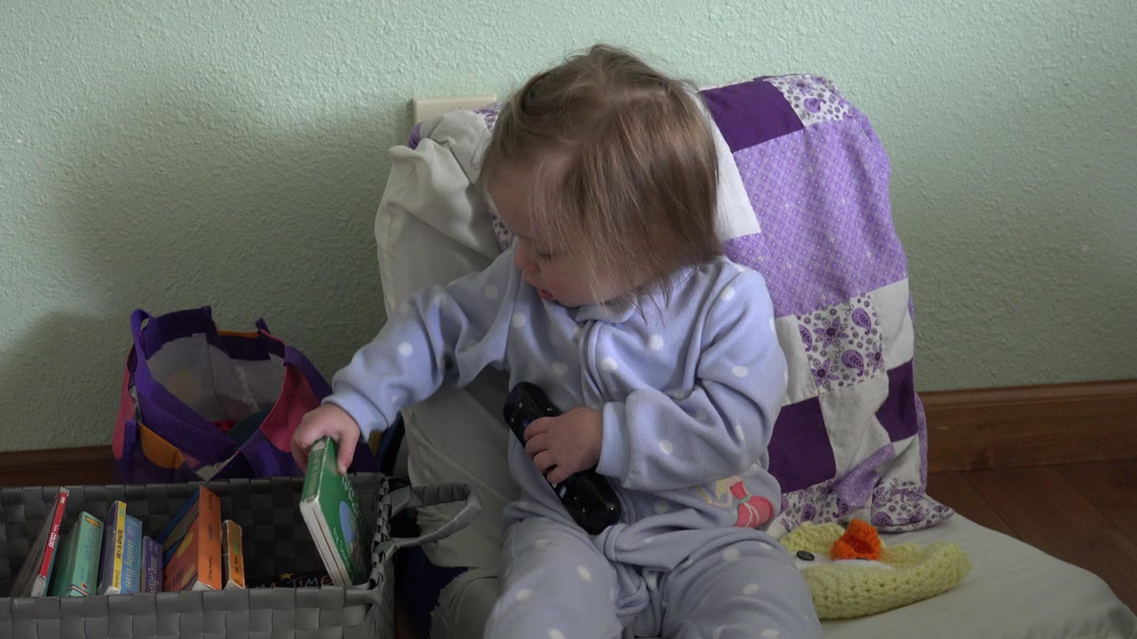 Toddler sitting beside a bin of books on a cushioned chair.