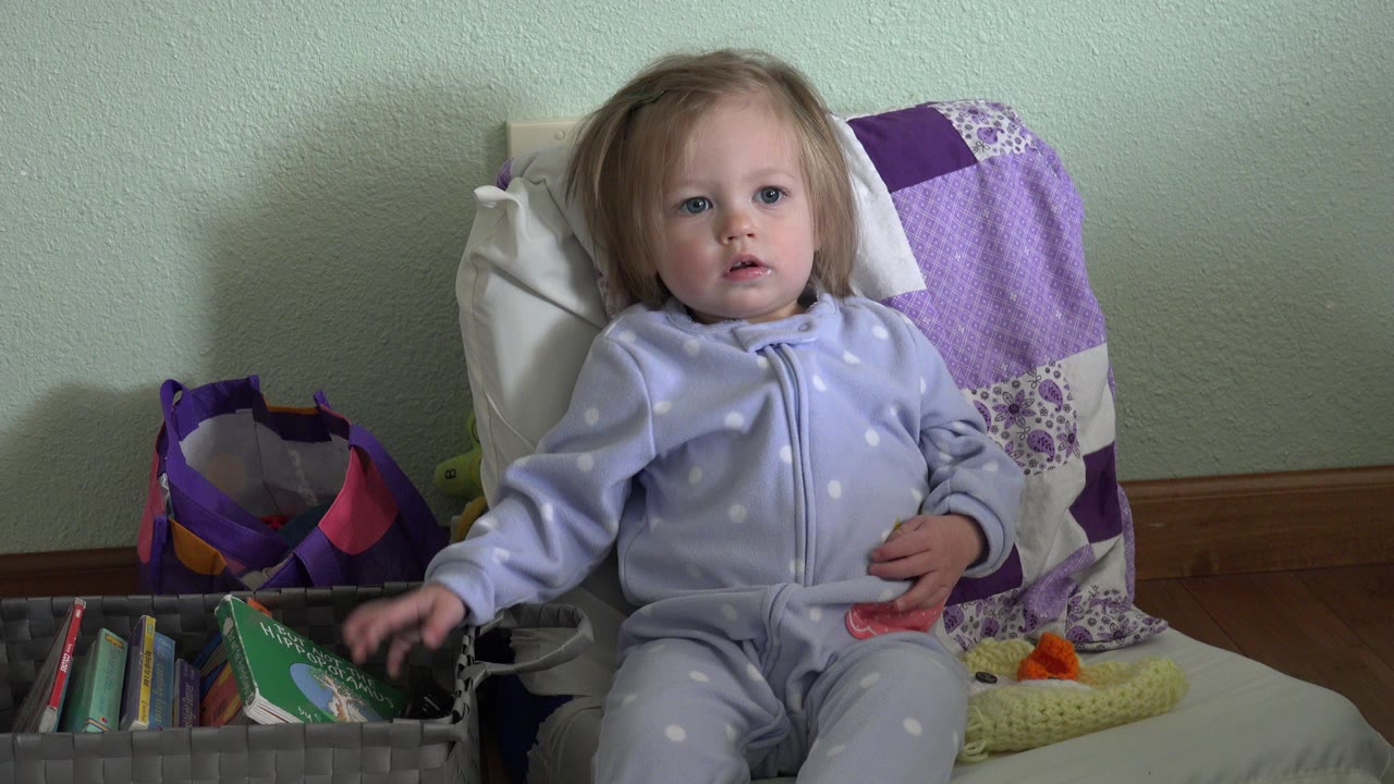Toddler in pajamas seated beside a basket of books.