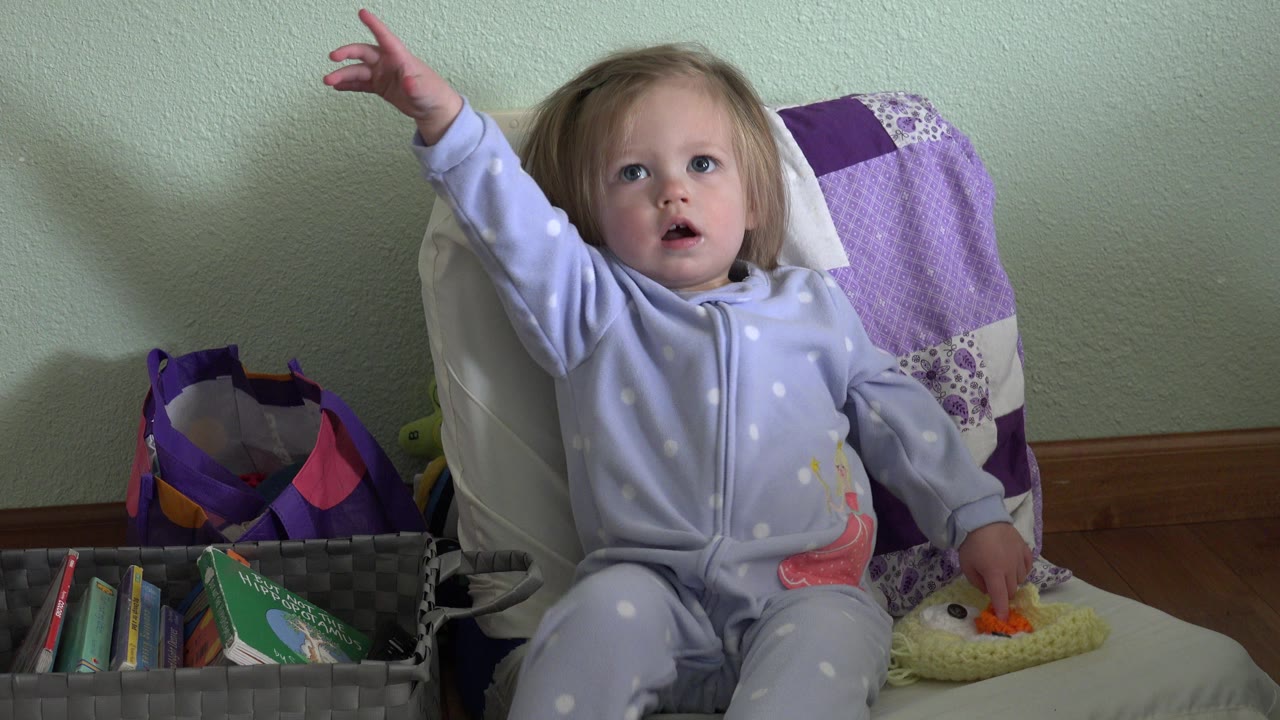 The child remains seated in the Westminster, Colorado home setting, looking toward the camera area with one arm raised and books visible in the lower-left basket.