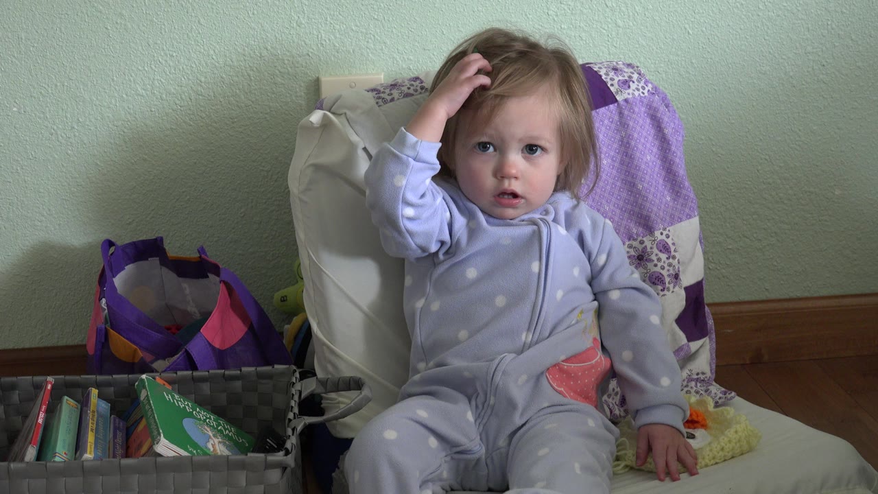Toddler in pajamas sits beside a basket of books.