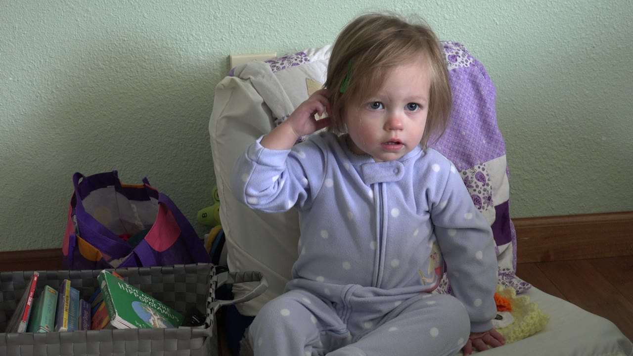 The child remains seated on the bed in the Westminster, Colorado interior, looking toward camera while her hand rests beside her ear.
