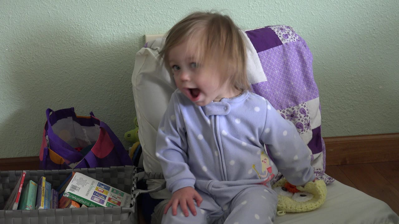 The baby remains seated in the Westminster, Colorado room, turned left with hair partly over the face and the toy basket visible in the lower foreground.