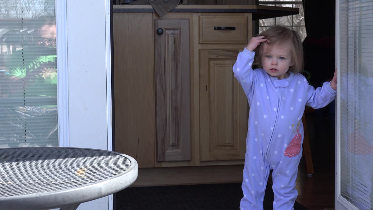 Toddler facing the camera with one hand on her head at the doorway.