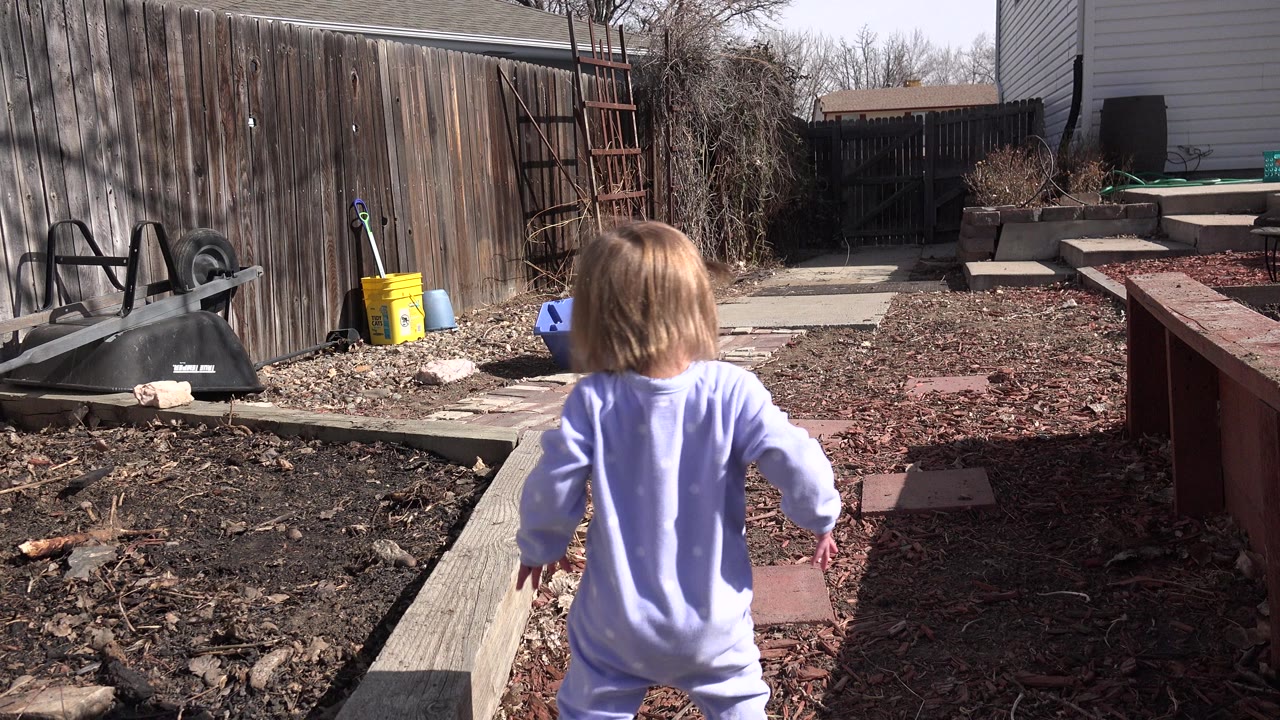 Child in light pajamas walking away through a backyard.