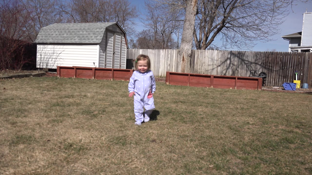 Young child walking across a backyard lawn.