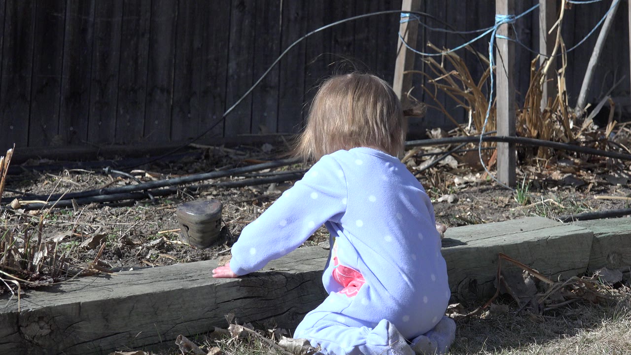 Child seen from behind beside a wooden garden ledge.