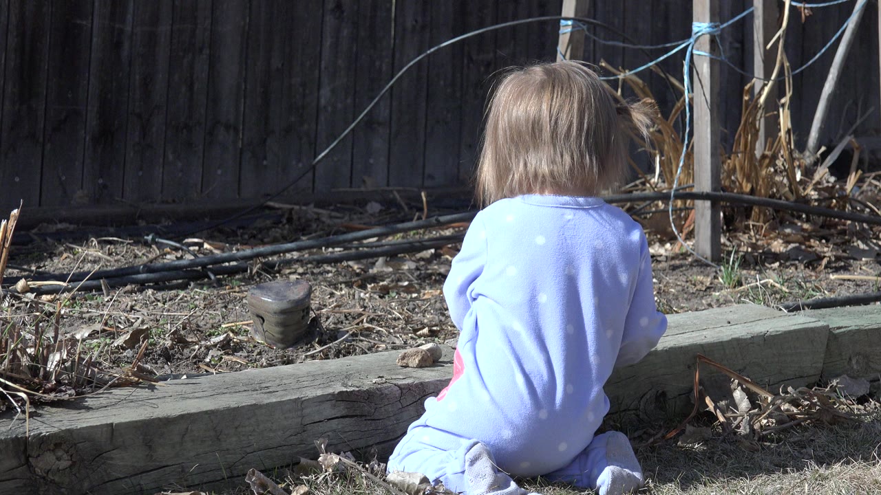 Child seated from behind beside a backyard garden border.