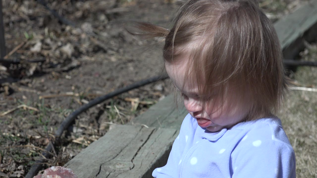 Blonde child looking down beside a wooden ledge outdoors.