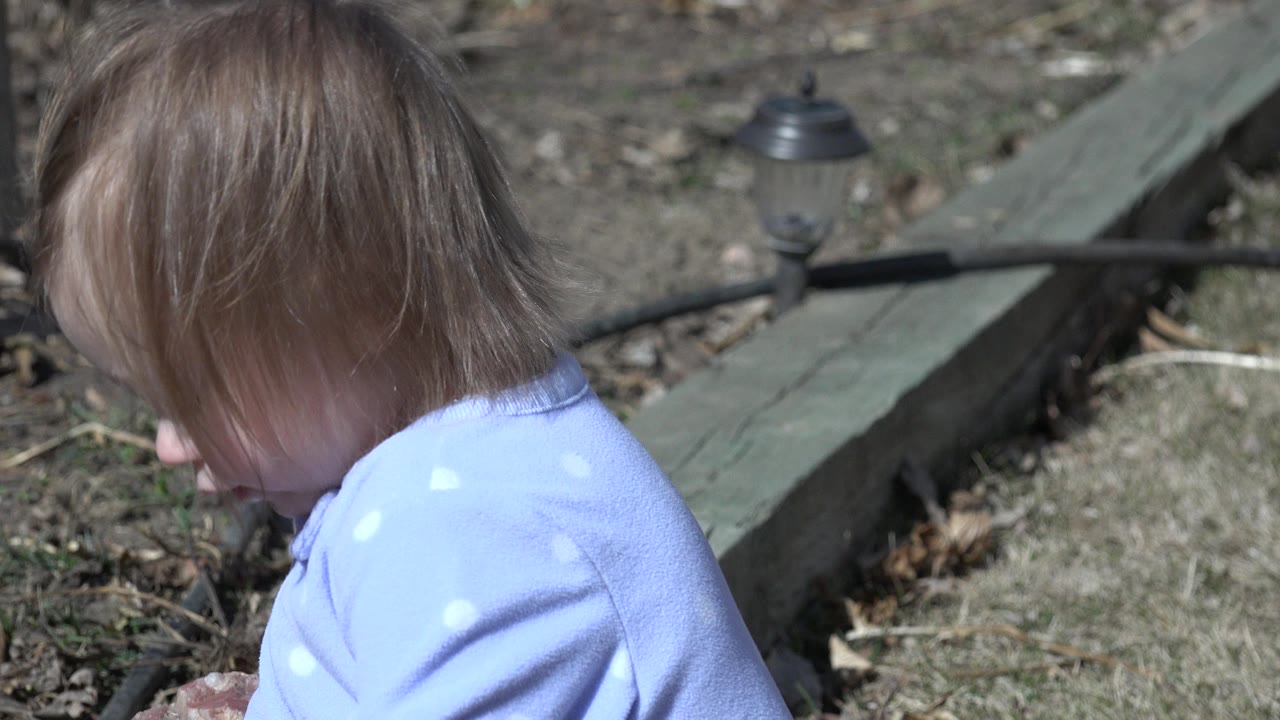 The child keeps their head lowered near the left side of frame, with the timber border, dry grass, and small path light remaining visible in the yard.