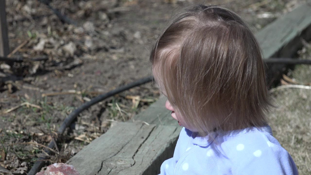 One second in, the child remains in left-facing profile in Westminster, Colorado, with hair covering much of the face and a weathered plank, dirt, leaves, and hose behind them.