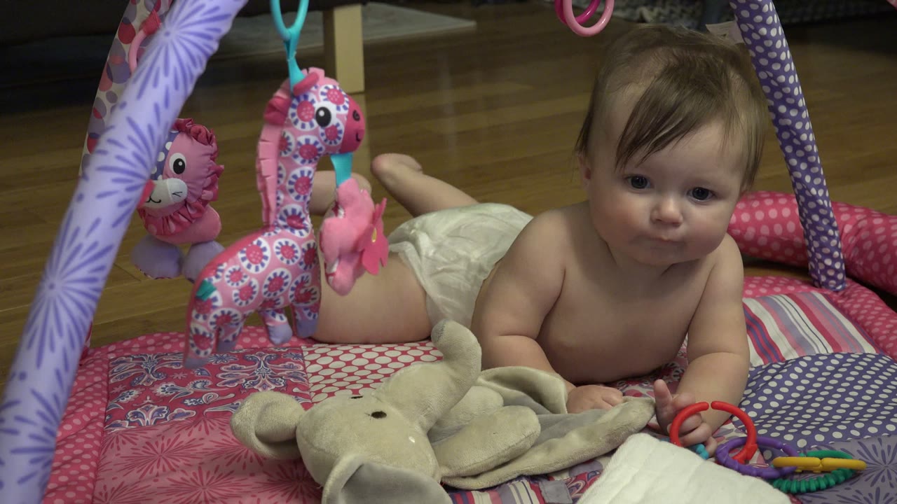 Baby on a patterned play mat with hanging toys.