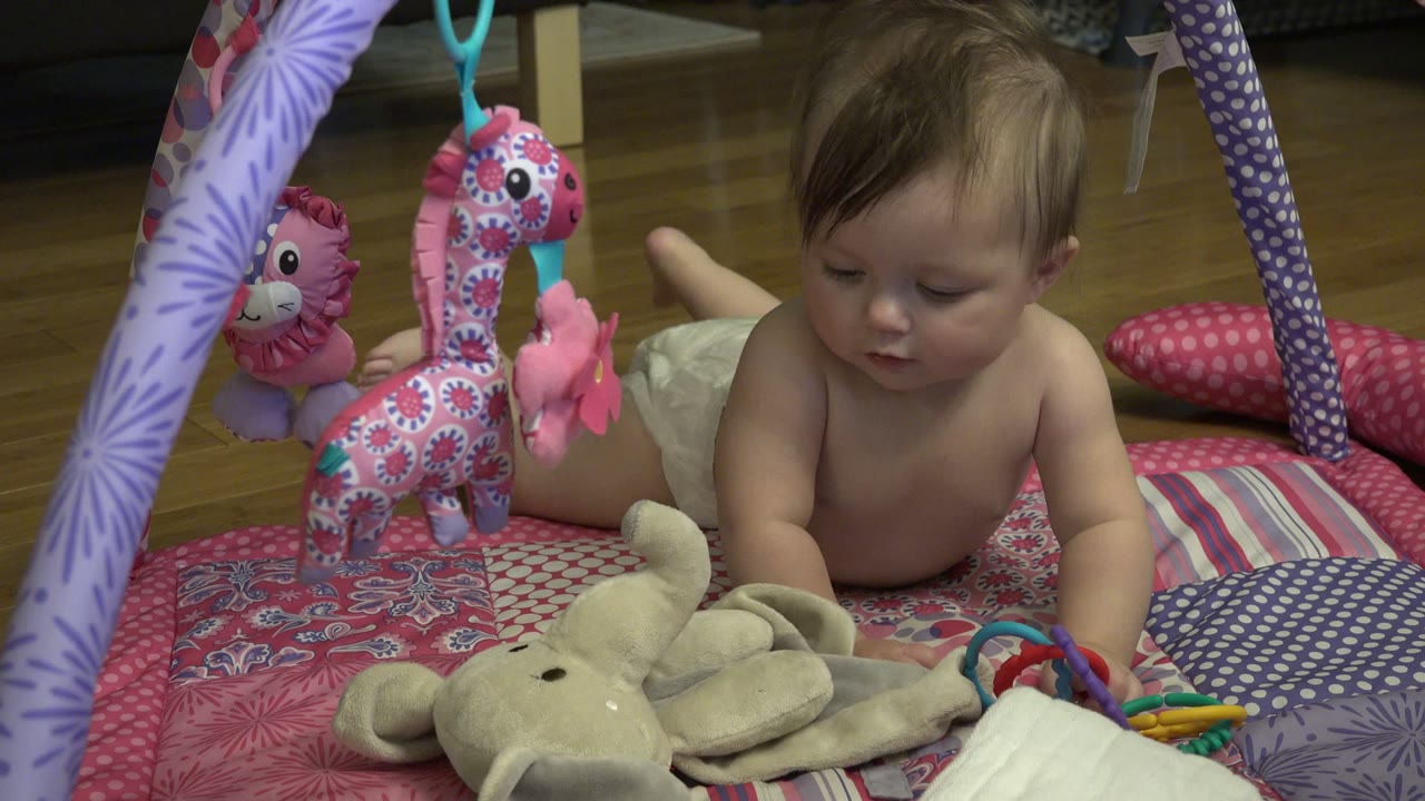 Baby lying on a padded play mat near plush toys.