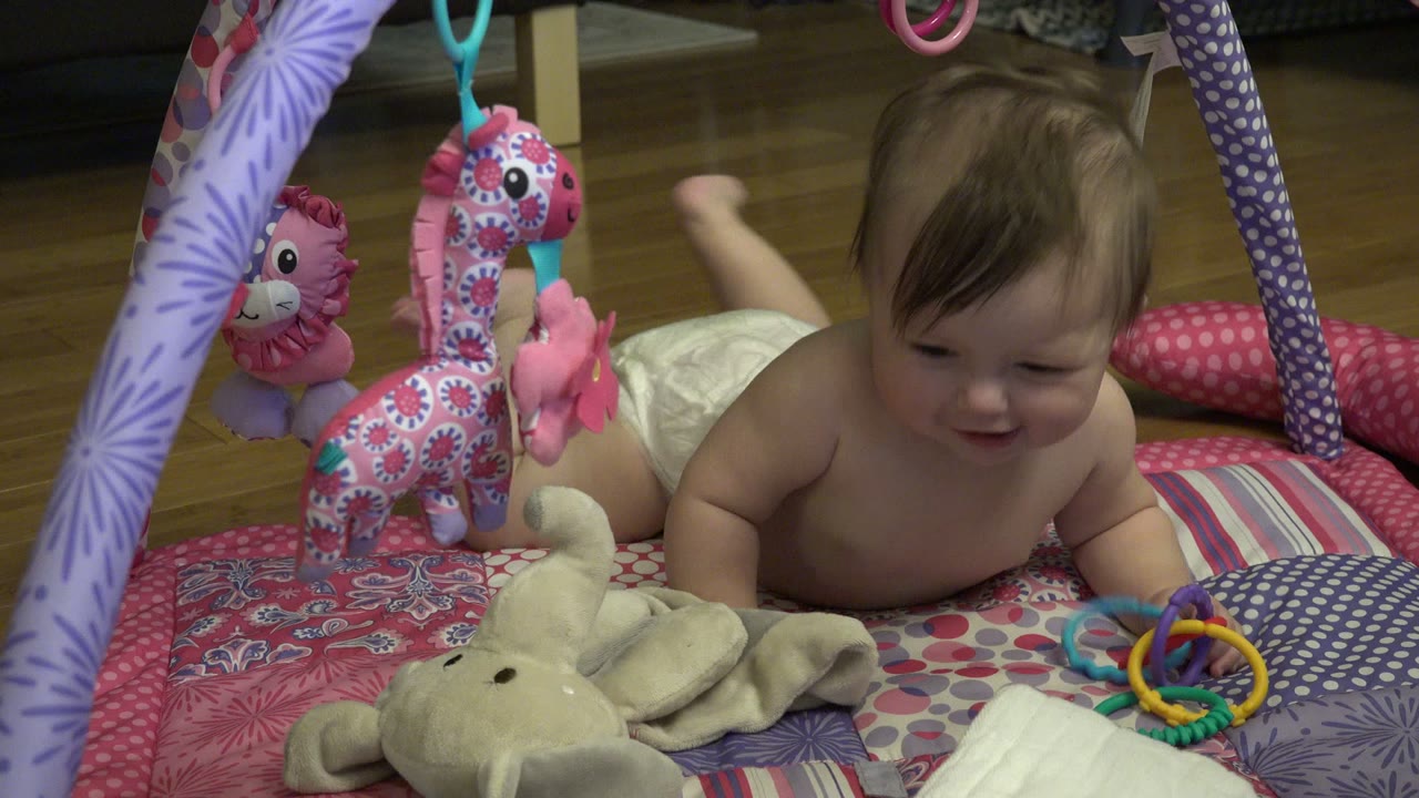 The baby in Westminster, Colorado leans forward with a small smile while a colorful ring rattle sits near one hand on the patterned mat.