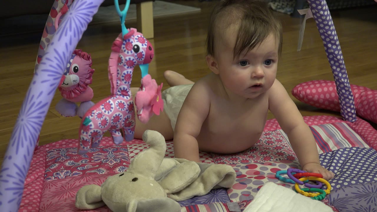 Baby lying on a patterned play mat beside hanging toys.