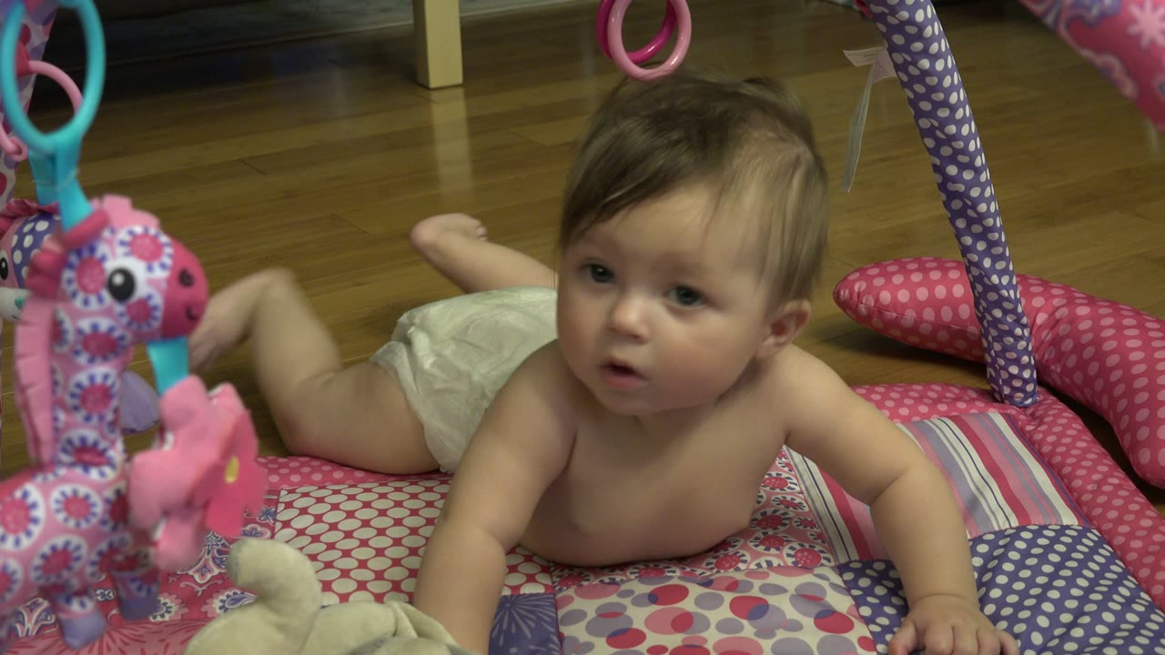 One second in, the baby stays on their stomach on the play mat in Westminster, Colorado, turning more toward the camera with a pink patterned toy hanging at left.