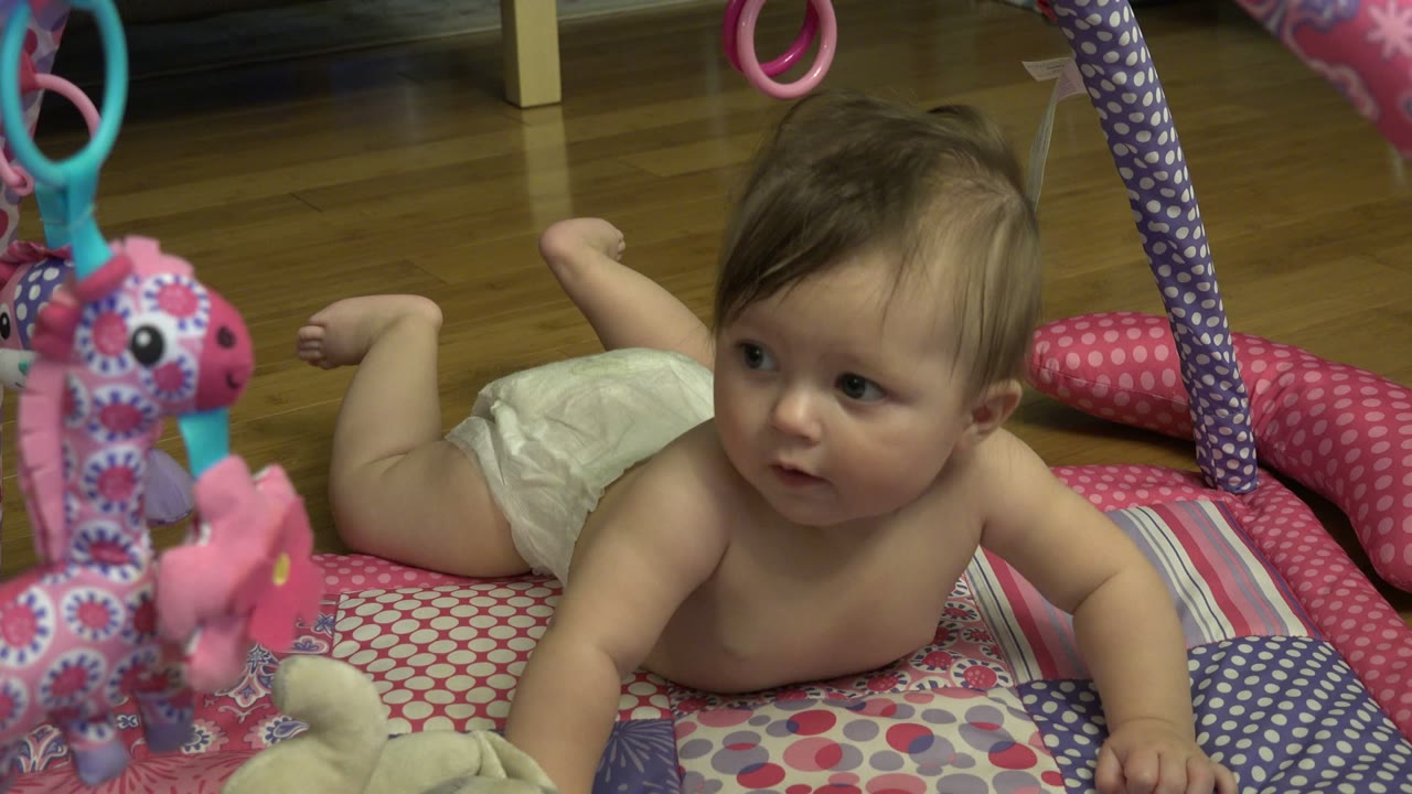 Baby lying on a colorful quilt under hanging toys.