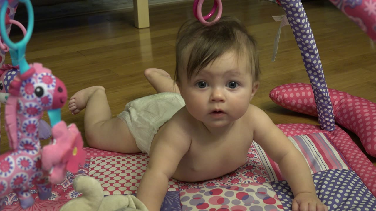 Baby lying on a patterned play mat under hanging toys.