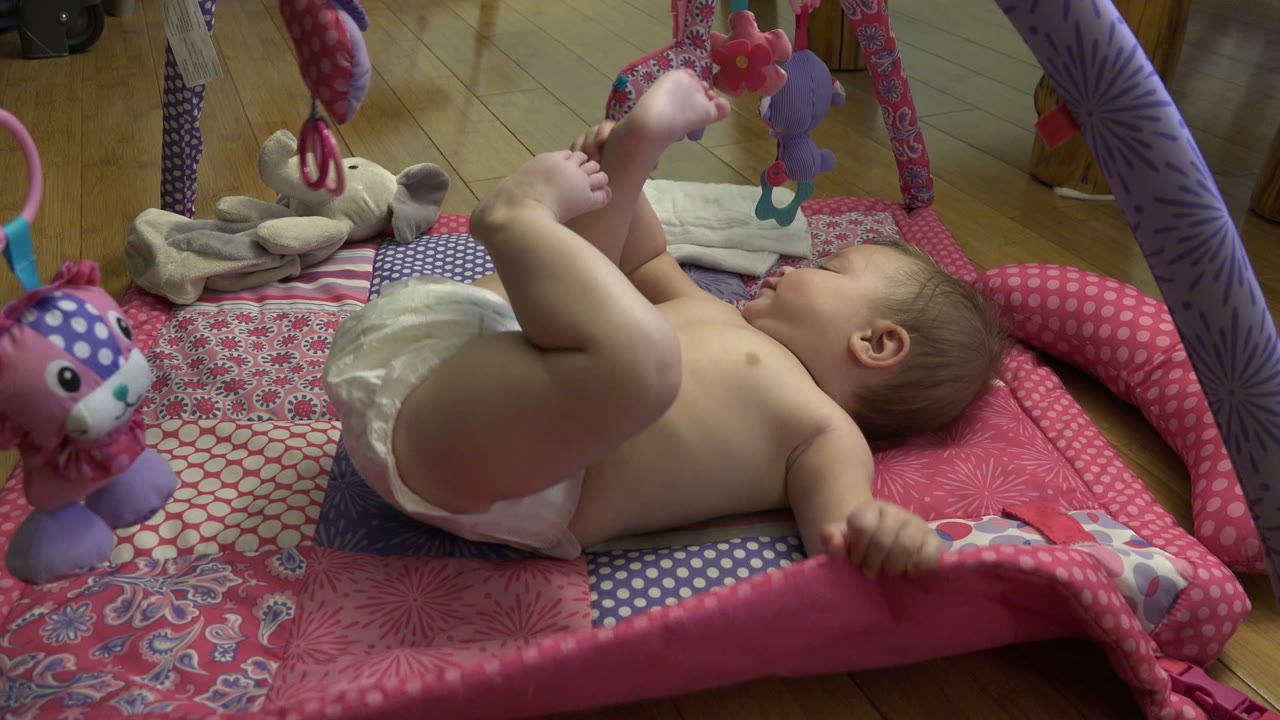 Baby lying on a patterned play mat with legs raised.
