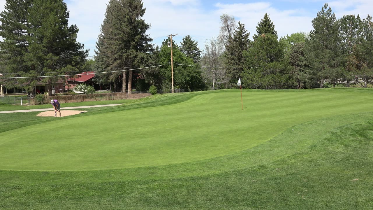At 0:01, the Denver golf course remains in a wide composition with a golfer near the left-side sand bunker and striped fairway grass stretching across the frame.
