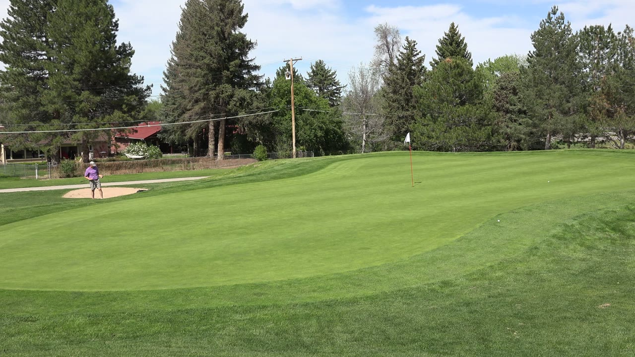 Wide golf course with a person near a sand bunker and green fairway.