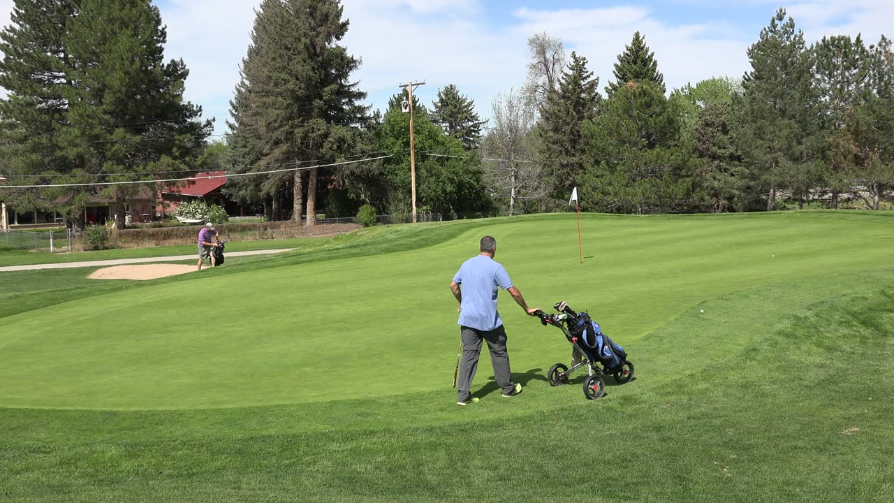 Wide Denver, Colorado golf course frame with one man standing near a push cart in the foreground area and another golfer near the sand bunker in the distance.