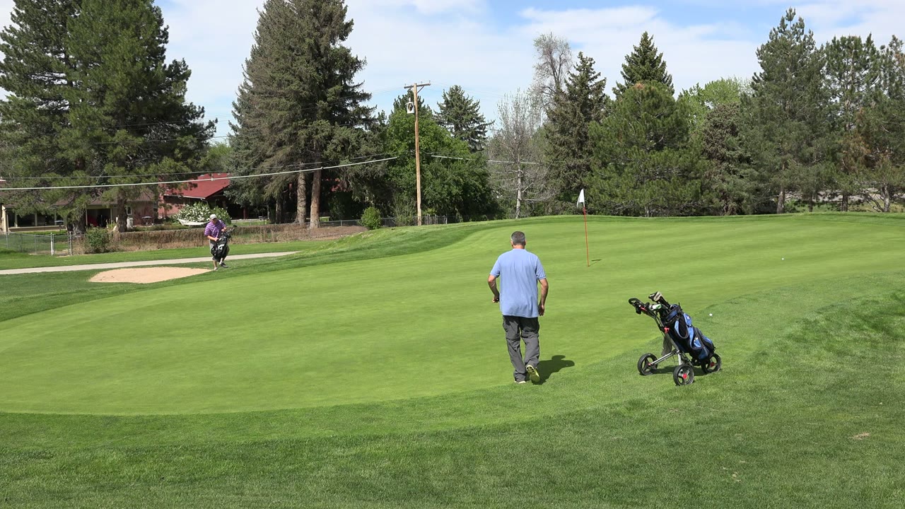 Denver, Colorado course view with the distant golfer closer to the bunker and the second man beside a wheeled golf bag on the trimmed green.