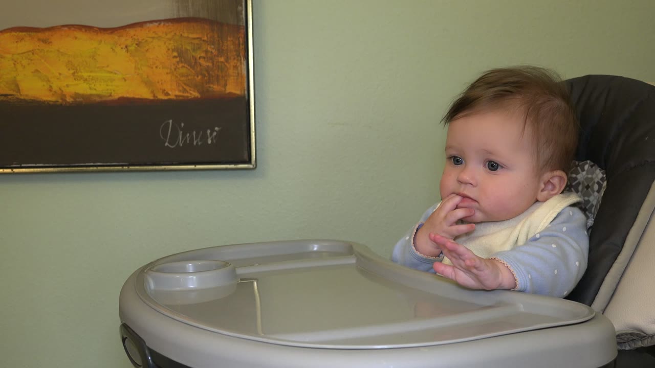 Baby seated in a high chair with fingers near mouth.