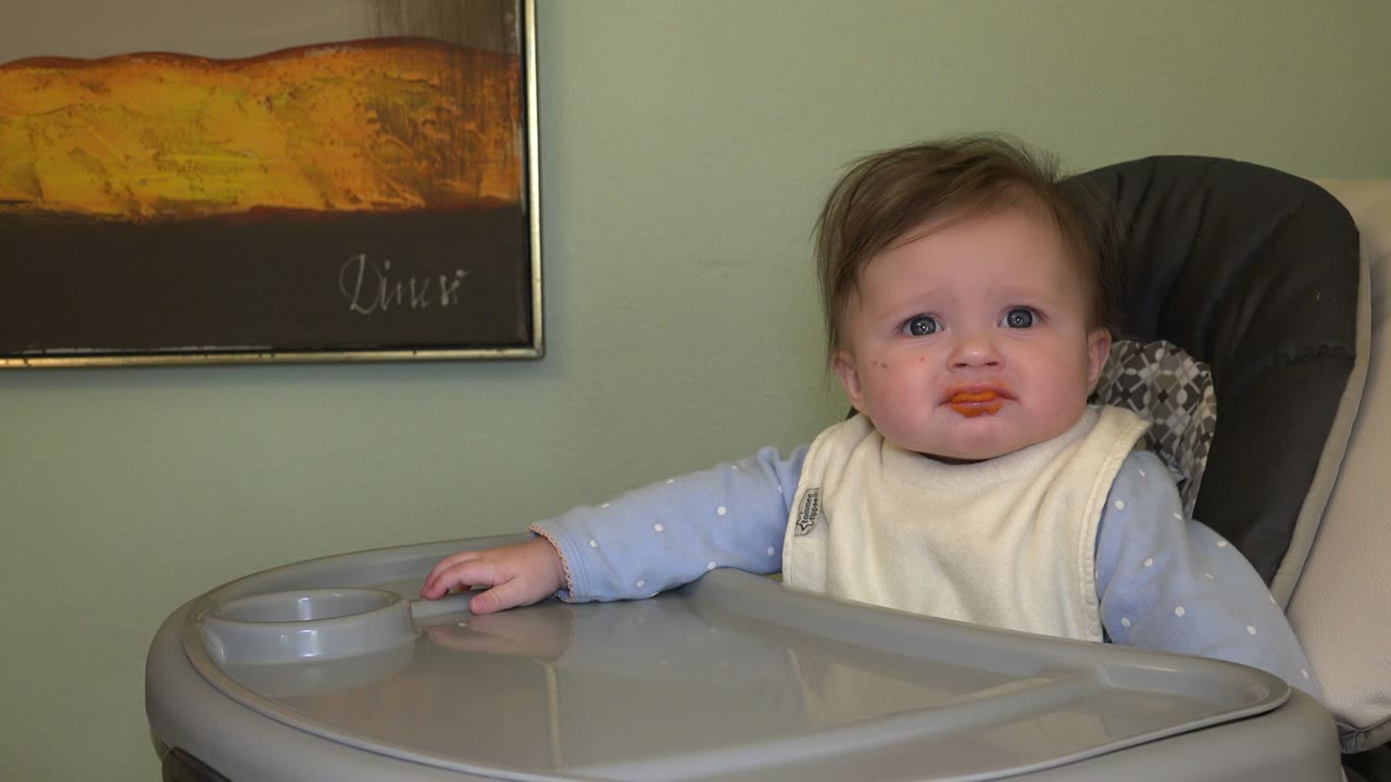 A baby in Westminster, Colorado looks straight ahead from a high chair, with one hand near the tray and food still visible around the mouth.