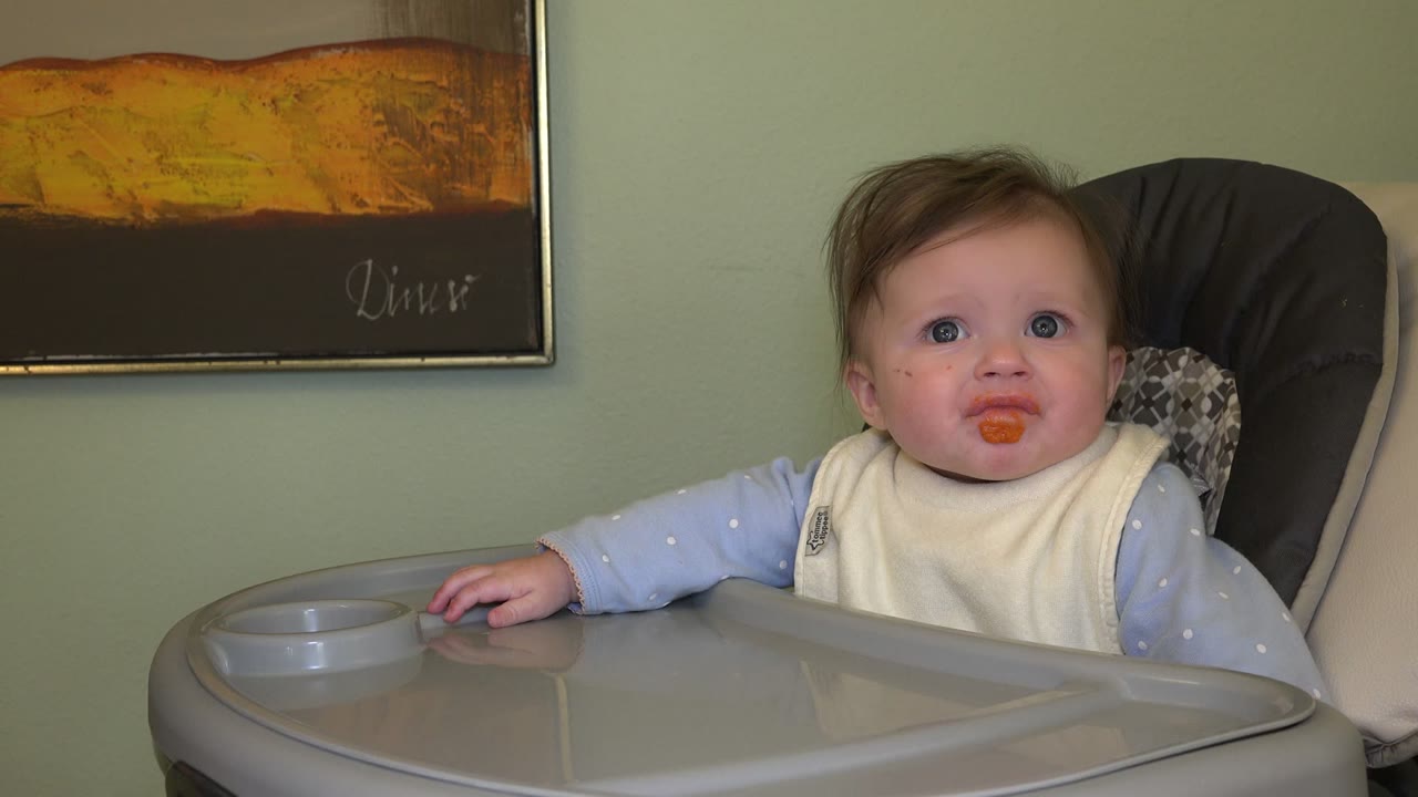 Baby in a high chair with orange food on the mouth.