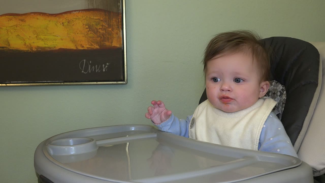 The baby remains in the high chair in Westminster, Colorado, looking off to the left with the tray edge filling the lower foreground and wall art above.