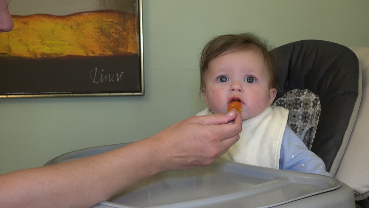 Baby in a high chair being fed with a spoon.
