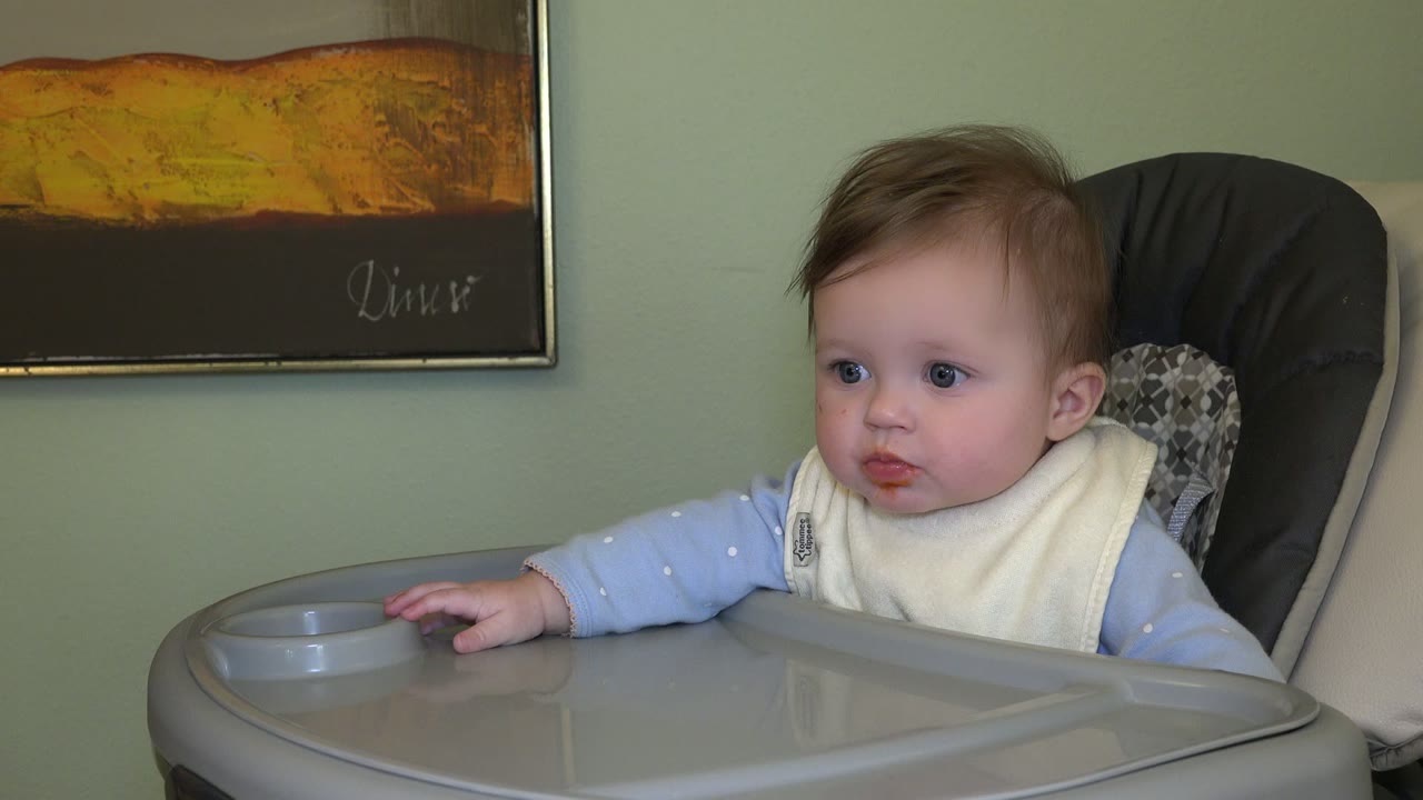 The baby remains seated in the Westminster, Colorado highchair scene, looking slightly left while one hand rests near the tray's cup holder.