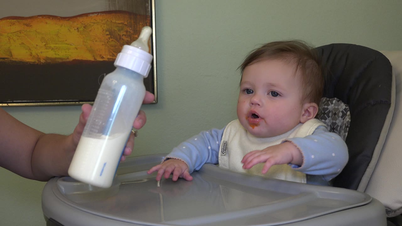 Baby in a high chair reaching toward a bottle.
