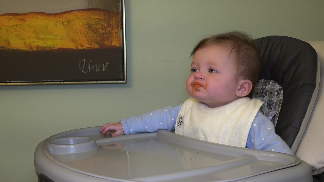 Baby in a high chair looking left with food around the mouth.