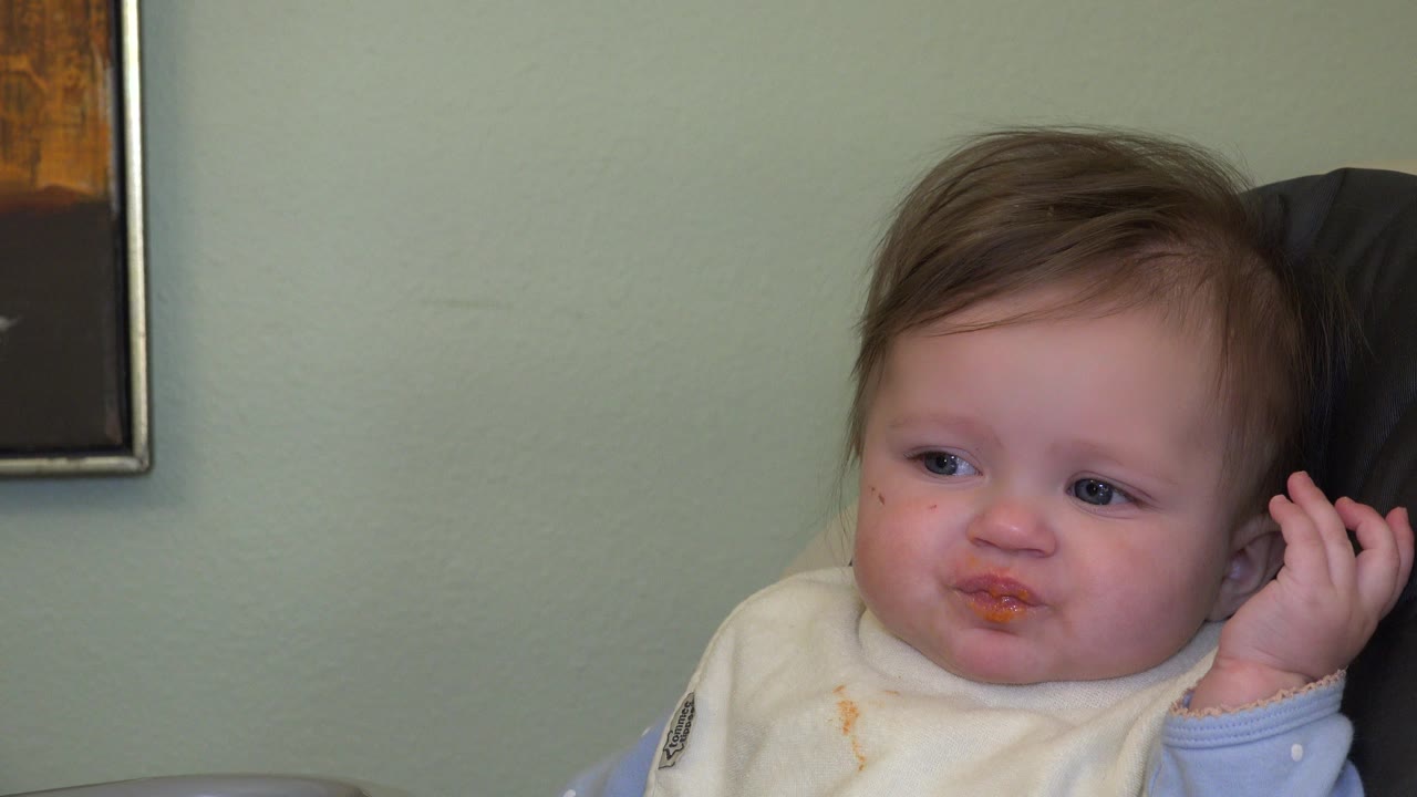 Young child in a bib with orange food around the mouth.