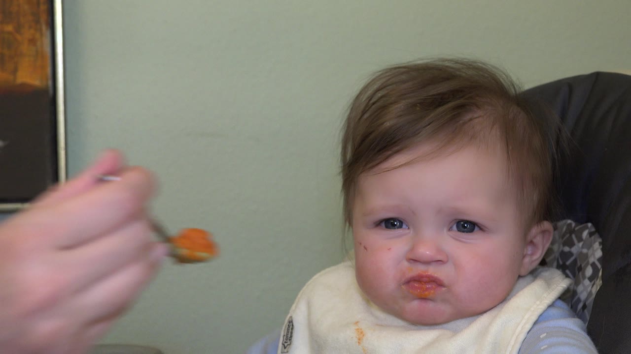Toddler in a high chair as a spoon approaches from the left.